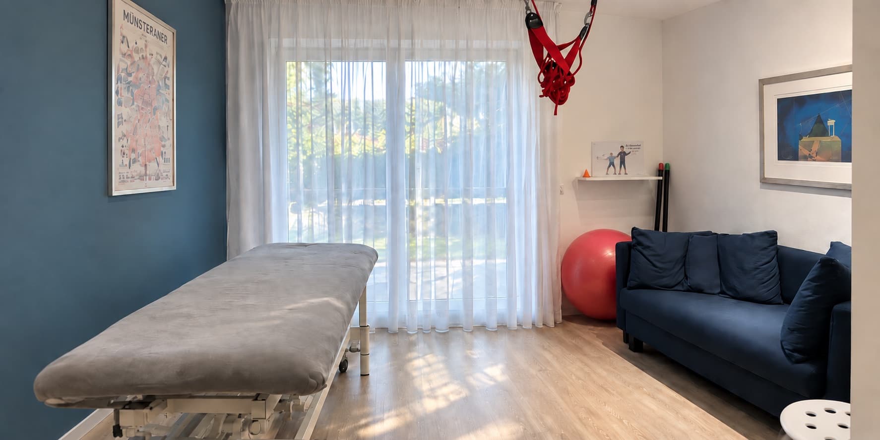 Behandlungsraum der Praxis mit Therapieliege, Fensterfront zum Garten und Sitzecke