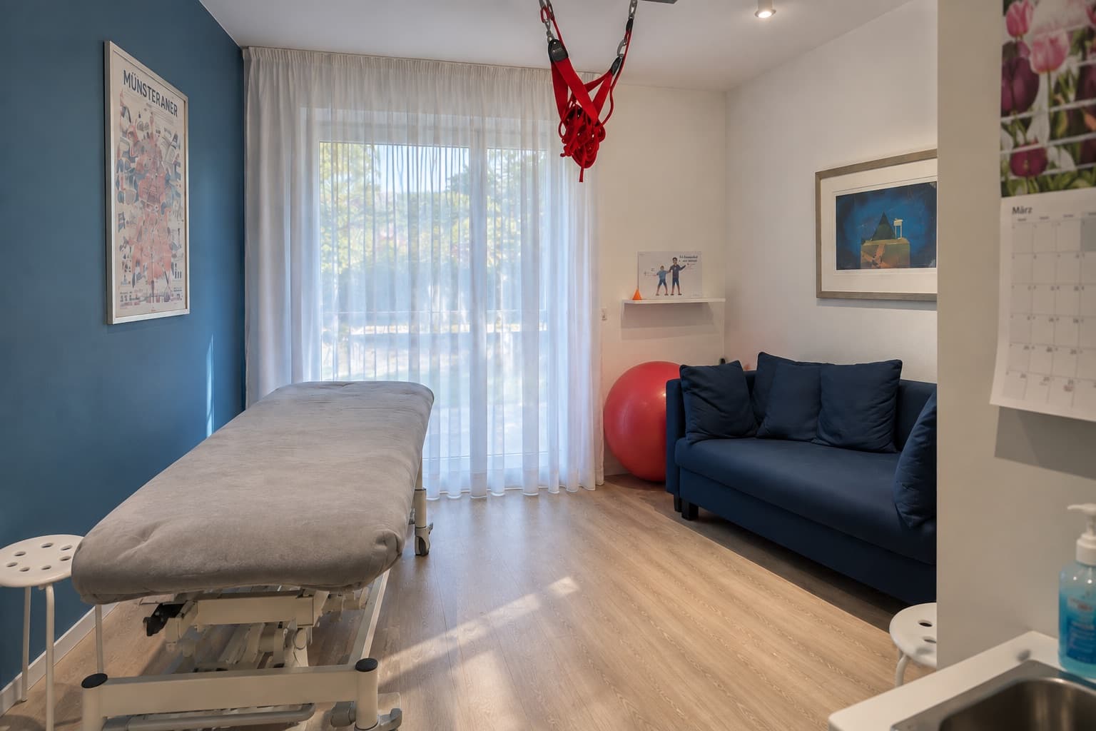Behandlungsraum mit Therapieliege, Fensterfront zum Garten und Sitzecke